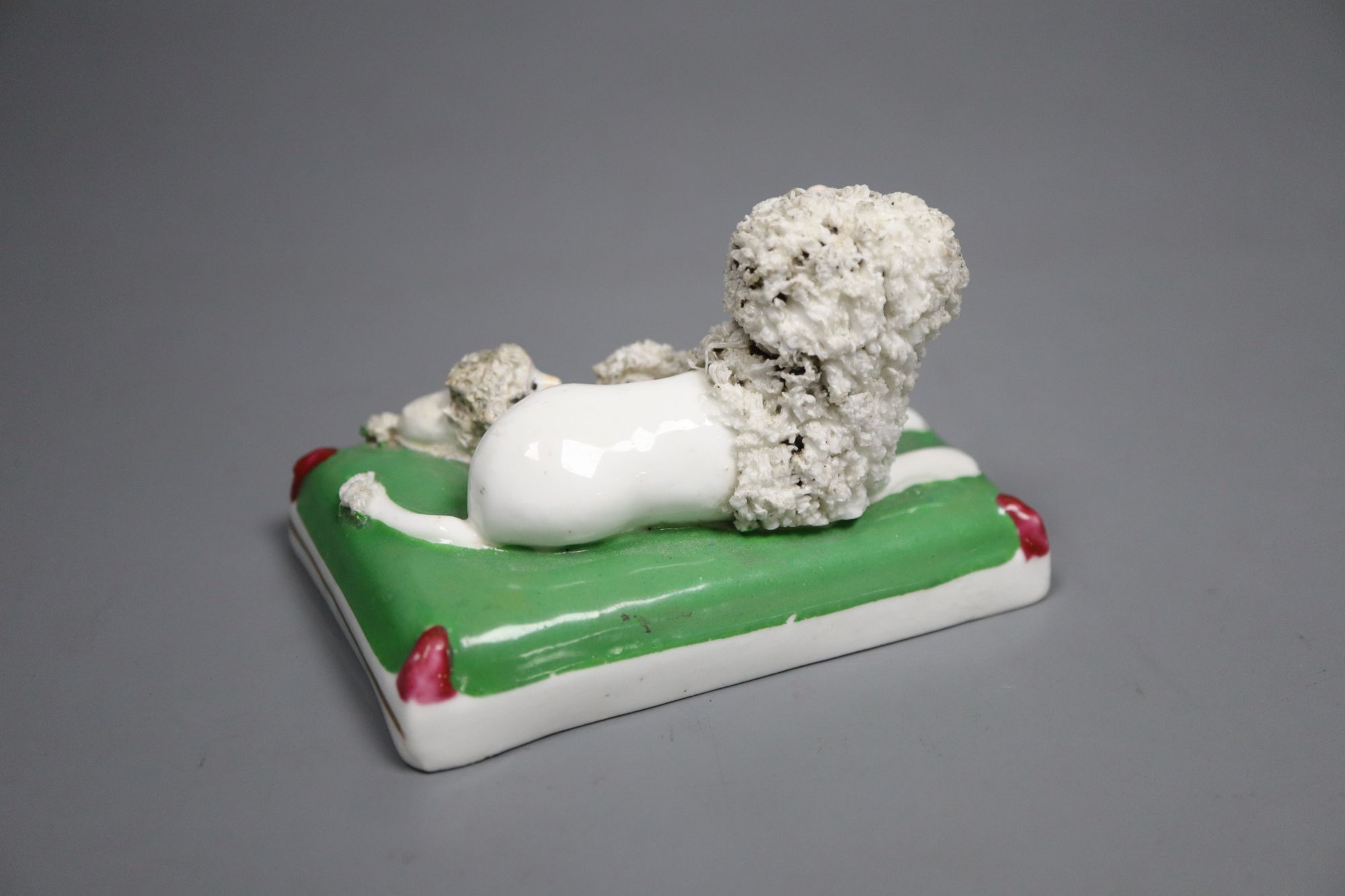 A Staffordshire porcelain group of a poodle and three puppies on a green cushion, c.1835-50, 9cm long